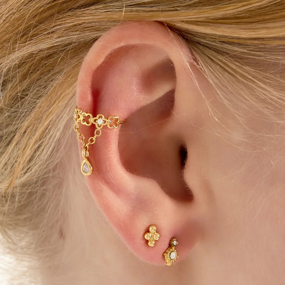 FRENCH RIVIERA Fleur de Chance kullanvärinen ear cuff -korvakoru, jossa apilamaiset kuviot ja riippuva kristallipisara.